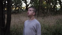 A depressed, sad young man, teenage boy on his knees praying in nature.