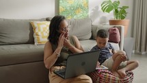 Mother multi-tasking, with son and using computer laptop at home. Candid authentic and real life mom working and parenting