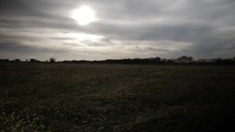Sun shines through clouds in a grass field at sunset or sunrise. Cinematic and dramatic slow motion shot.