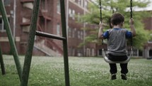 A father pushes his small, happy child on a swing at a park in cinematic slow motion on Father's Day.
