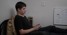 Young teen boy, teenager sitting in his bedroom on his bed studying for a test for high school class.