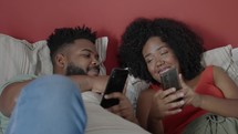 Happy young couple in bed on their phone on social media