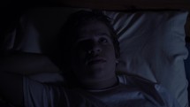 Young man laying in bed unable to sleep. A teenager in his bedroom lays on his bed at night sleepless and awake.