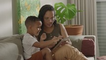 Latina mother and preschool son playing on tablet at home together