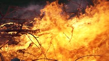 Closeup of hot, blazing flames of camp fire burning wood logs and tree branches in cinematic slow motion.