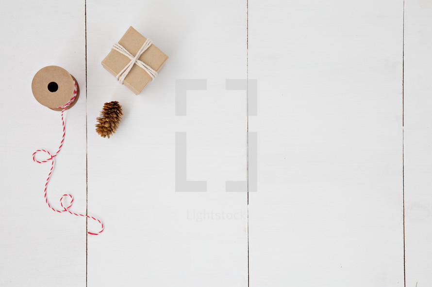 spool of thread, pine cones, and gifts wrapped in brown paper on white background 