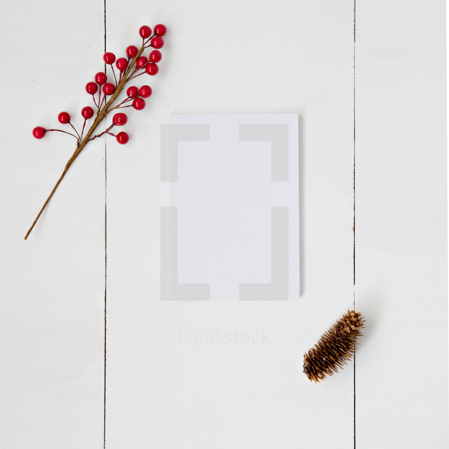red berries, pine cone, and blank white paper 