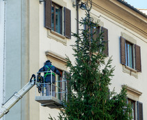 Christmas Tree Installation in large square. Worker on lifting platform takes care of the installation of lights.