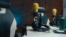 Desk with microphone, headphones, clipboard with worksheet, travel mug and chair in podcast recording studio. No people, close-up view