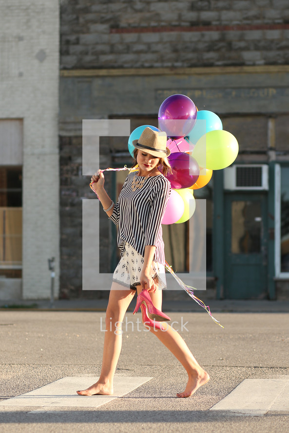 a teen girl walking carrying her shoes and balloons