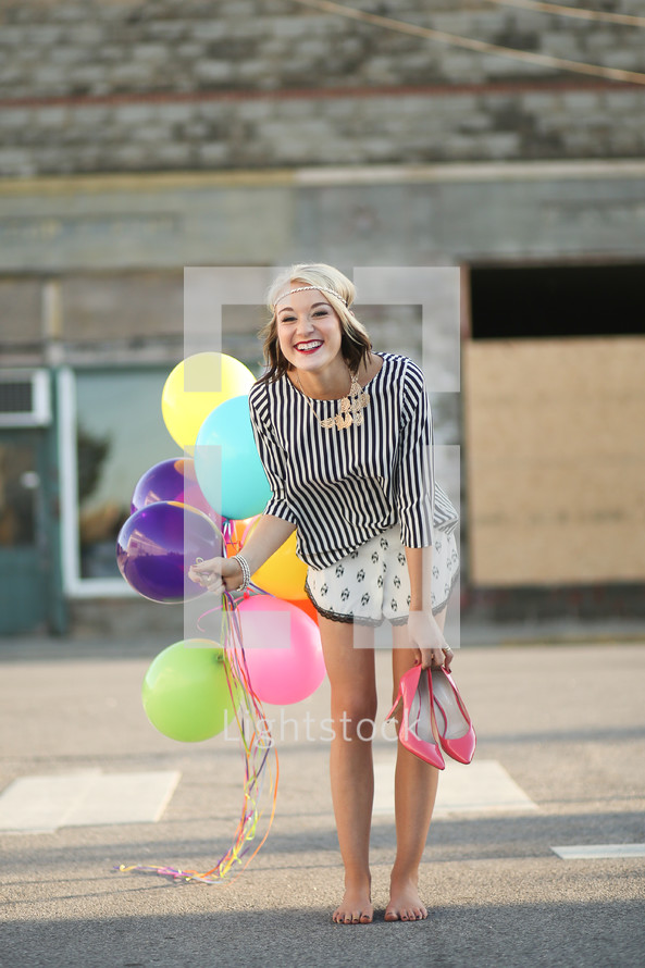a teen girl carrying her shoes and holding balloons 