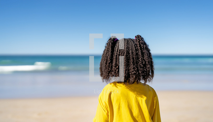 girl with back to camera standing on a beach