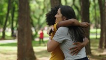 Two happy young girls hug each other. Females embracing, laughing and excited. Woman friendship, walk in city park outdoors. 
