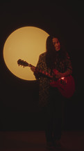 Young Musician Playing Guitar in Dark Studio with Spotlight