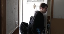 Teenager with backpack walking out front door of house. A teen boy, high school student walking to school or running away from home.