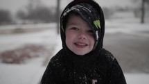 Happy young boy playing in cinematic slow motion in the snow while it's snowing outside on Christmas morning smiling at the camera.