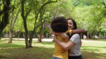 Two happy young girls hug each other. Females embracing, laughing and excited. Woman friendship, walk in city park outdoors. 