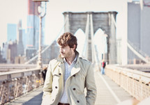 man in a trench coat walking on a bridge