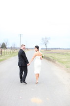bride and groom holding hands walking down a country road
