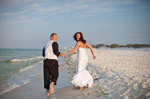 bride and groom holding hands and running on a beach