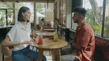 Young woman speaking with male friend when meeting at the cafe and having summer cocktails. Medium long shot, side view
