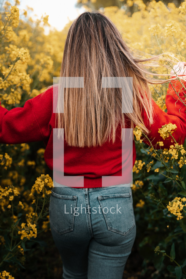 Spring fashion, woman walking through yellow flowers rapeseed field