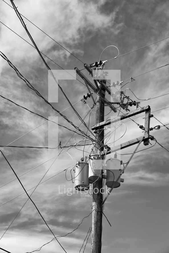 Telephone pole, transformers and electrical wires against a cloudy sky.