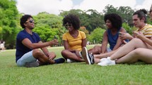 A Group of Multiethnic Young friends sitted in the Park, Talking and Laughing. Diverse Friends watching funny videos on mobile smartphone