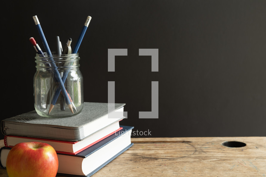 apple, books, and pens on a desk 