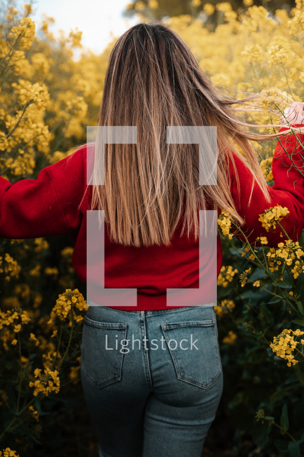 Spring fashion, woman walking through yellow flowers rapeseed field