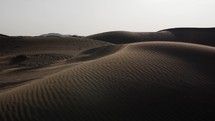 Middle eastern desert, nature landscape. Sand blowing in wind over desert sand dunes in evening desert sunlight in cinematic slow motion.
