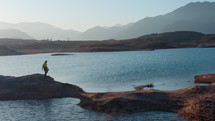 Drone shot of man running on stones across Potrerillos Dam lake located in Argentina. Adventure tourism, wanderlust concepts
