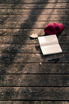 a ball cap, open journal, and pen on a wood deck 