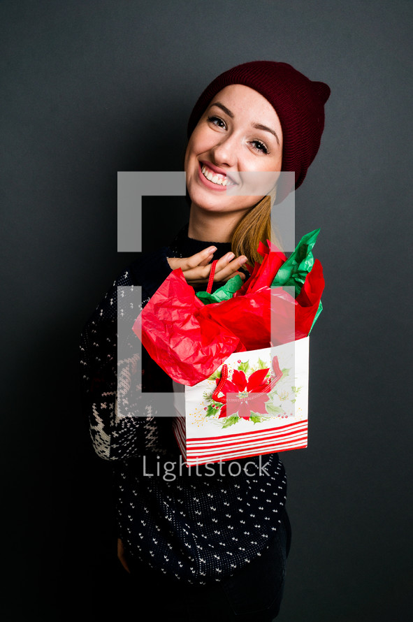 a young woman holding a Christmas gift bag
