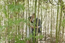 A groom kisses his bride on the forehead behind some bamboo trees