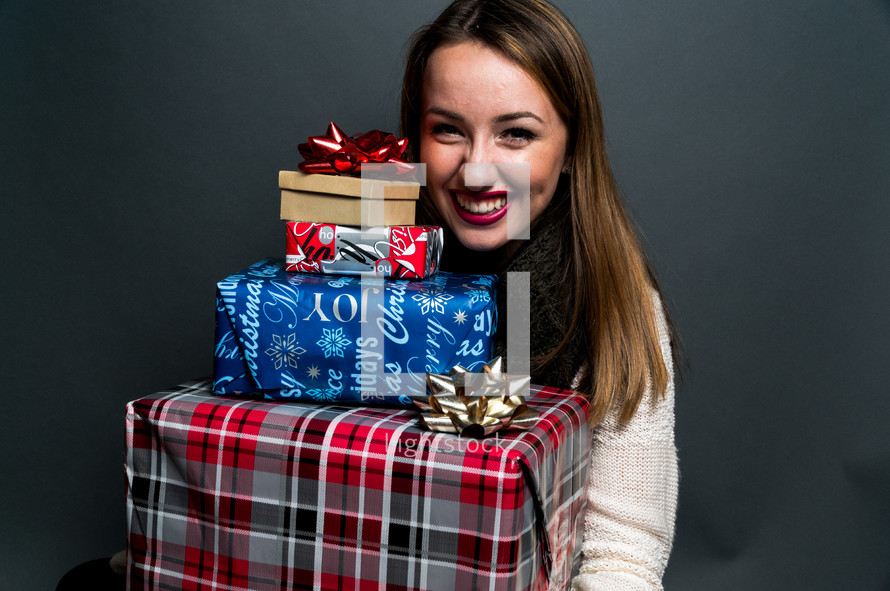 a teen girl holding a stack of Christmas gifts 