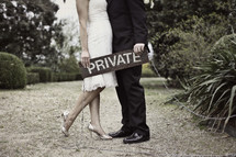 torso of bride and groom holding a private sign
