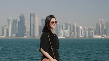 Tourist woman walking at MIA park with Doha skyline behind
