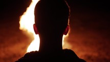 A young man watching a large fire with engulfing flames in cinematic slow motion.