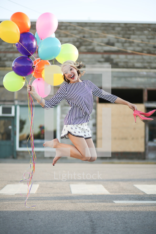 teen girl jumping holding balloons and shoes 