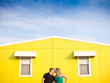 man and woman kissing in front of a yellow house