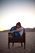 woman sitting on a chair in the parched earth of a desert