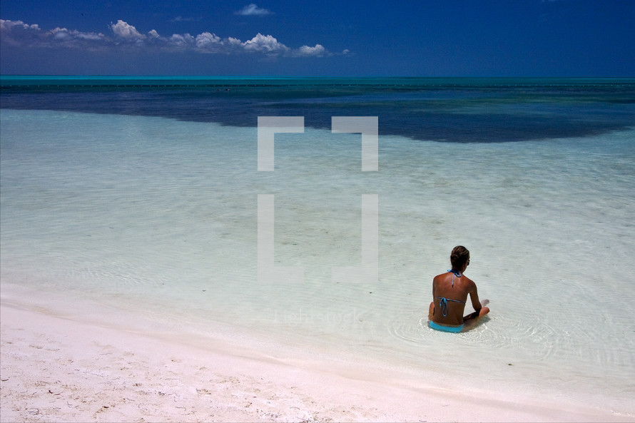 woman sitting in calm water relaxing at the beach 