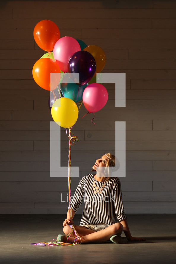 a woman holding balloons sitting on the floor 