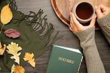 woman's arms and fall leaves on a green scarf and Holy Bible 