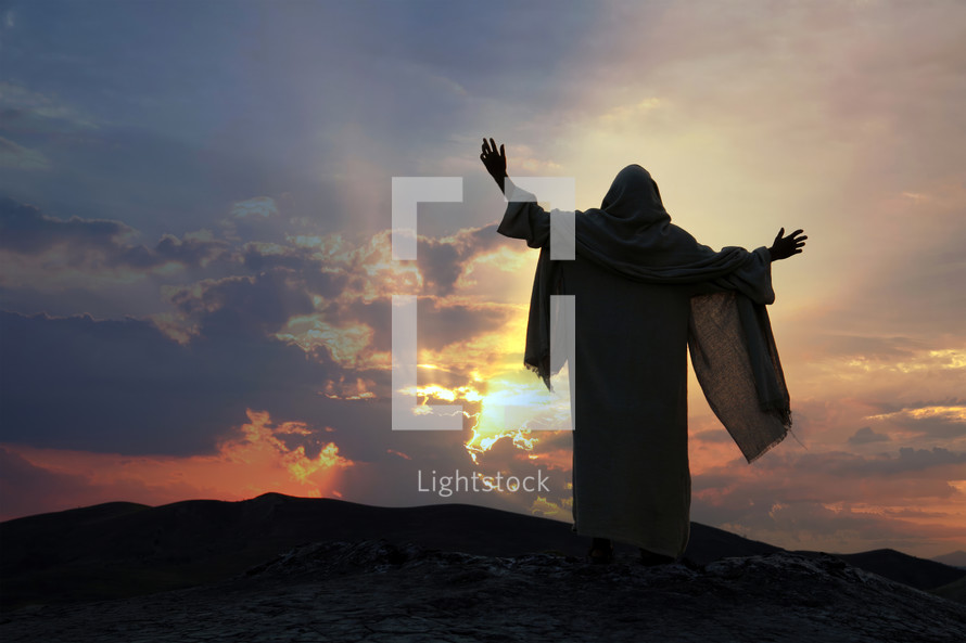 Jesus praying alone with raised hands on a hill at sunset. Biblical concept.
