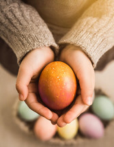 Young childs' hands holding a single colored easter egg for the holiday.