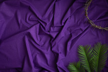Crown of thorns and palm leaves on purple cloth background