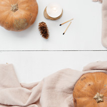 candle, matches, scarf, pumpkin, fall leaves, pine cones, and beanie on a white wood background 