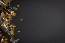 Champagne bottle, champagne flutes and gold streamers and confetti on a black background with copy space